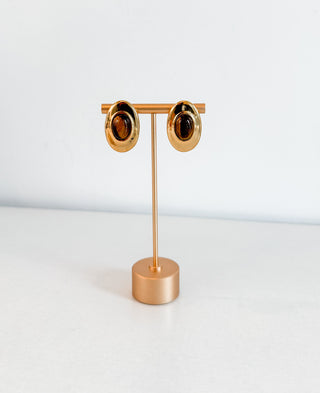 Gold earring stand with two gold earrings on a white background