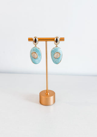 Turquoise earrings on a gold stand against a white background