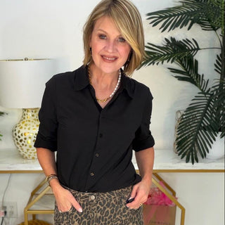 Woman wearing a black shirt and leopard print shorts in a room with plants and decor.